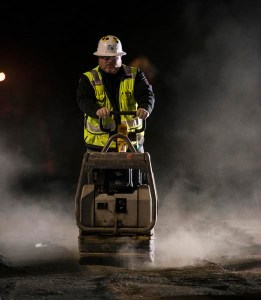Unknown worker uses gravel compactor to slat ten gravel that was disturbed during a night time highway closure. 