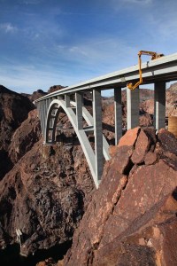 The long arm of a Nevada DOT bridge inpsection truck descends down and around the Mike O'Callaghan-Pat Tillman Memorial Bridge (Hoover Dam Bypass) delivering bridge inspectors to their work on a routine biennial bridge inspection. The concrete-steel composite arch bridge looms 840 feet above the Colorado River and is the 2nd largest bridge in the United States at 1,900 feet in length.