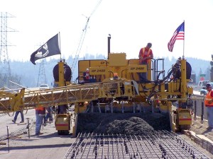 A crew on the Oregon Department of Transportation’s Interstate 5 Willamette River Bridge project in Eugene, Ore., carefully guides a large paver to form the continuously reinforced concrete pavement, creating a 12-foot-wide roadway. Additional workers follow behind to “float” a final hand finish that ensures a smooth, quiet ride.