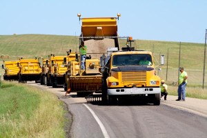 Applying a chip seal to Highway 53 in Lyman Co. are SDDOT employees Rod Lillebo, riding the chip spreader; Gary Hovey, operating the oil distributor; and Todd Hanson and Tim Huffman watching to make sure the oil and sand are being dispensed and distributed properly.