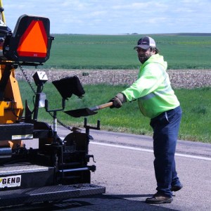 Loren Haynes, Highway Maintenance Worker from Martin shovels asphalt behind the paving machine as the crew works to repair highways in south central South Dakota. Asphalt patching is essential for not only the safety of the traveling public, but also extends the usable life of the pavement.